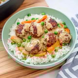 Ein Teller Reis mit Fleischbällchen in cremiger Sauce, garniert mit Karotten und Erbsen.