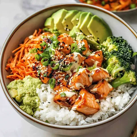 Eine Schüssel mit Reis, gebratenem Lachs, Karotten, Brokkoli, Avocado, Sesam und einer cremigen Sauce.