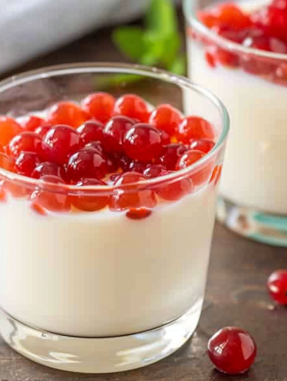 A glass of yogurt with red berries on top.