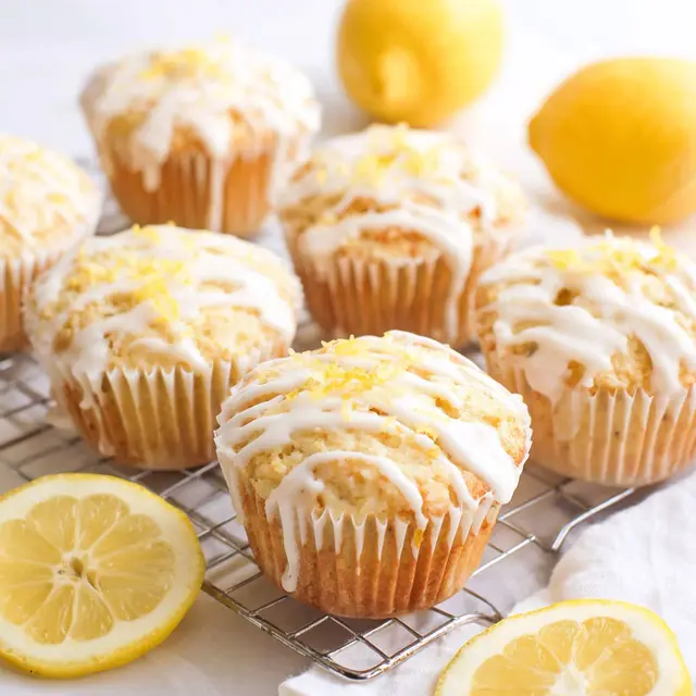A tray of lemon ricotta muffins with a lemon wedge on top.