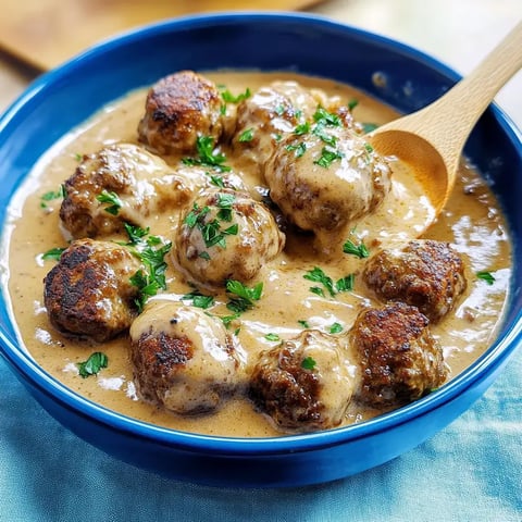 Eine Schüssel mit Fleischbällchen in cremiger Sauce, garniert mit frischer Petersilie.