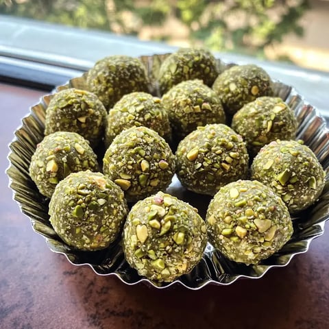 Eine silberne Schale mit einer Vielzahl grüner, kugeliger Süßigkeiten, die mit gehackten Pistazien bestreut sind.