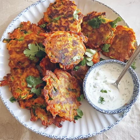 Ein Teller mit knusprigen vegetarischen Pfannkuchen, garniert mit Koriander, neben einer Schüssel mit Joghurtsauce.