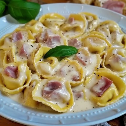 Eine Schüssel mit Tortellini in cremiger Sauce, garniert mit einem Blatt frischem Basilikum.