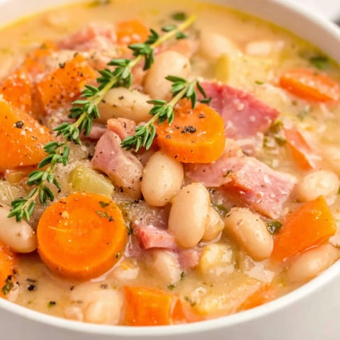 A white bowl filled with soup containing ham and beans.