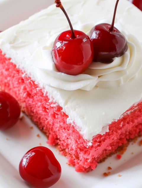 A slice of cherry sheet cake with cherries on top.