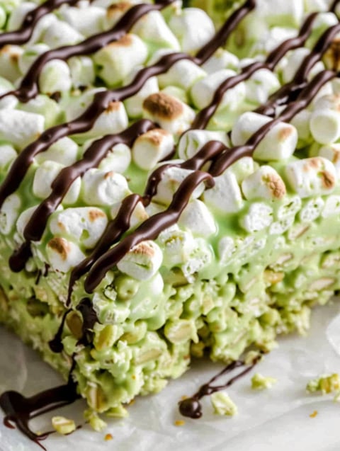 A slice of pistachio rice krispie treats with dark chocolate drizzled on top.