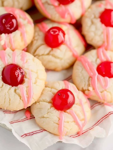 A plate of cookies with cherries on top.